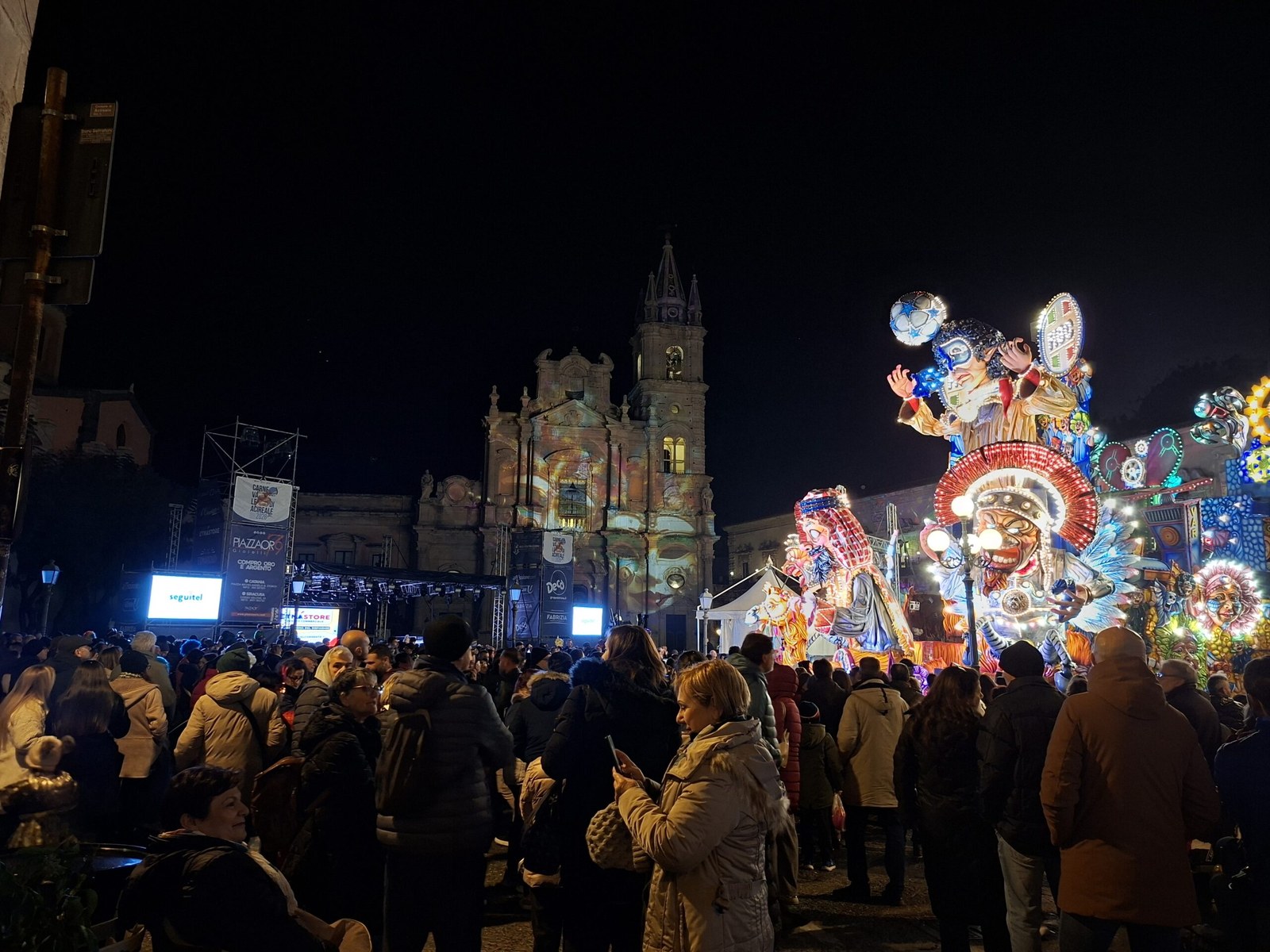 Crowd in Piazza Duomo at the Carnevale di Acireale 2026 with paper-mache float and the Basilica dei Santi Pietro e Paolo behind