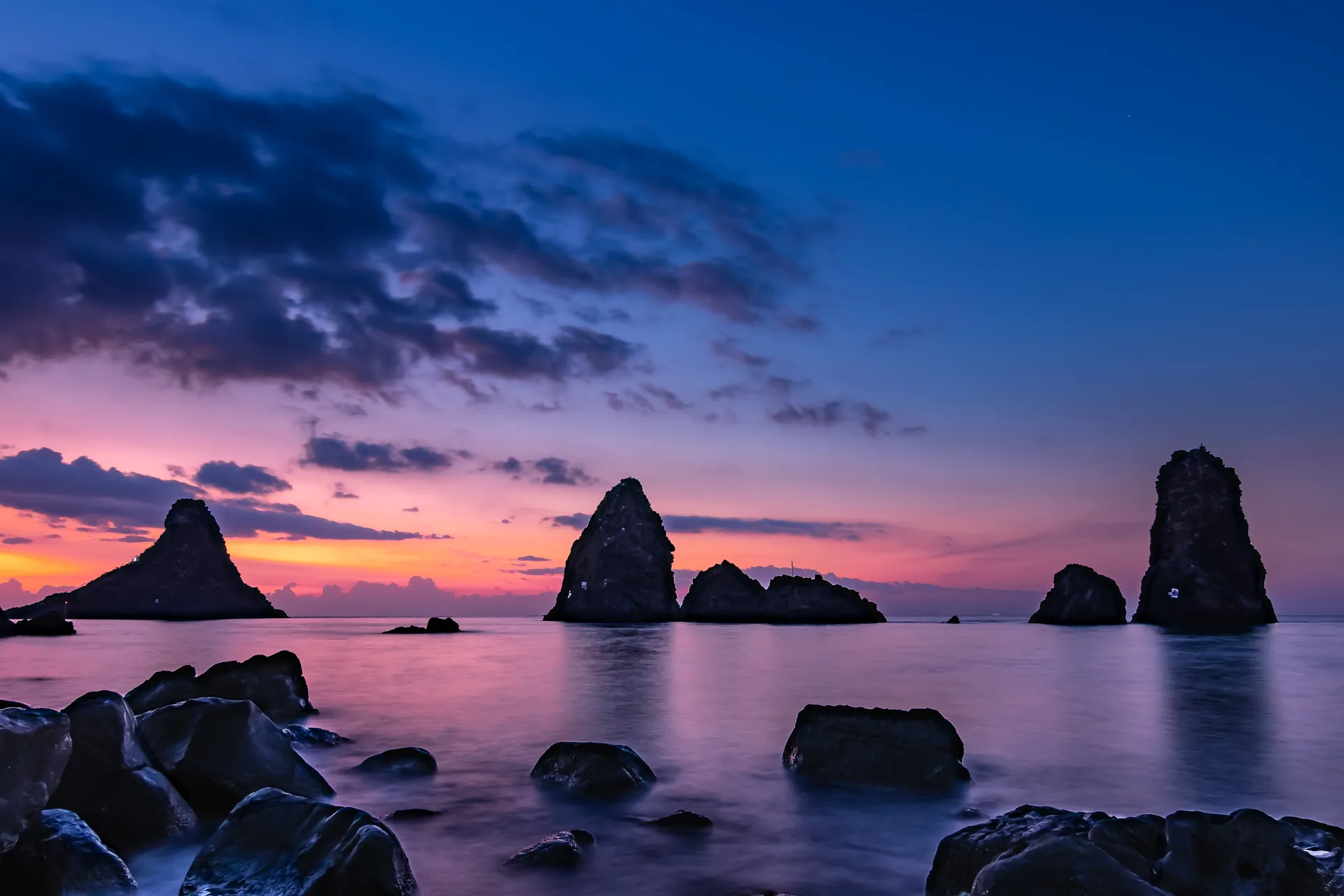 Faraglioni dei Ciclopi ad Aci Trezza all'alba con la luce dorata che illumina le rocce laviche emergenti dal mare ionio